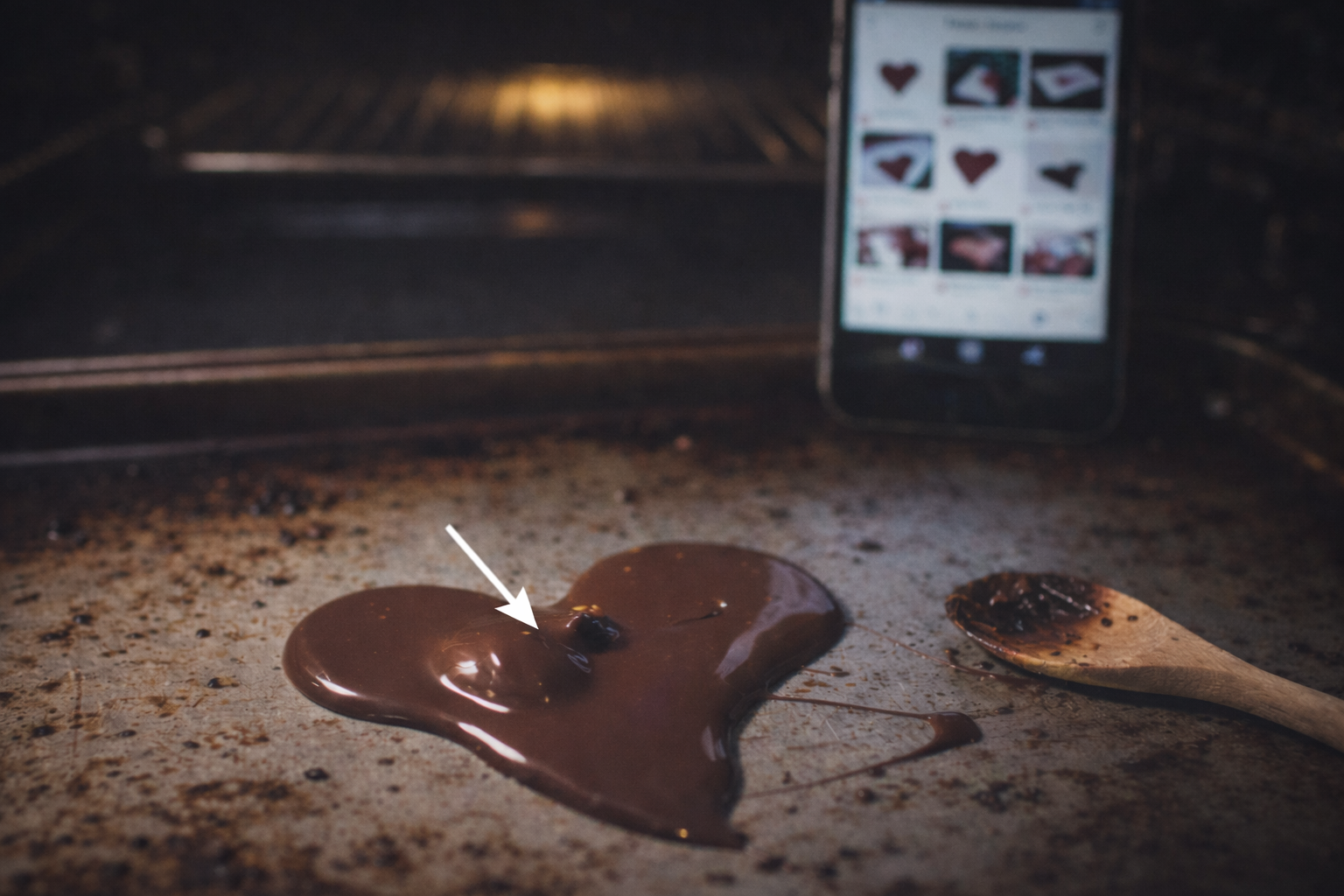 Melting chocolate heart on a baking tray with phone in background and a white arrow pointing at the heart, representing modern dating life, slow fade, and Valentine’s Day memes.