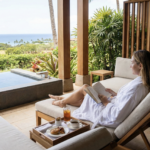 Woman on a solo wellness retreat reading on a terrace overlooking the ocean with a plunge pool and breakfast tray.